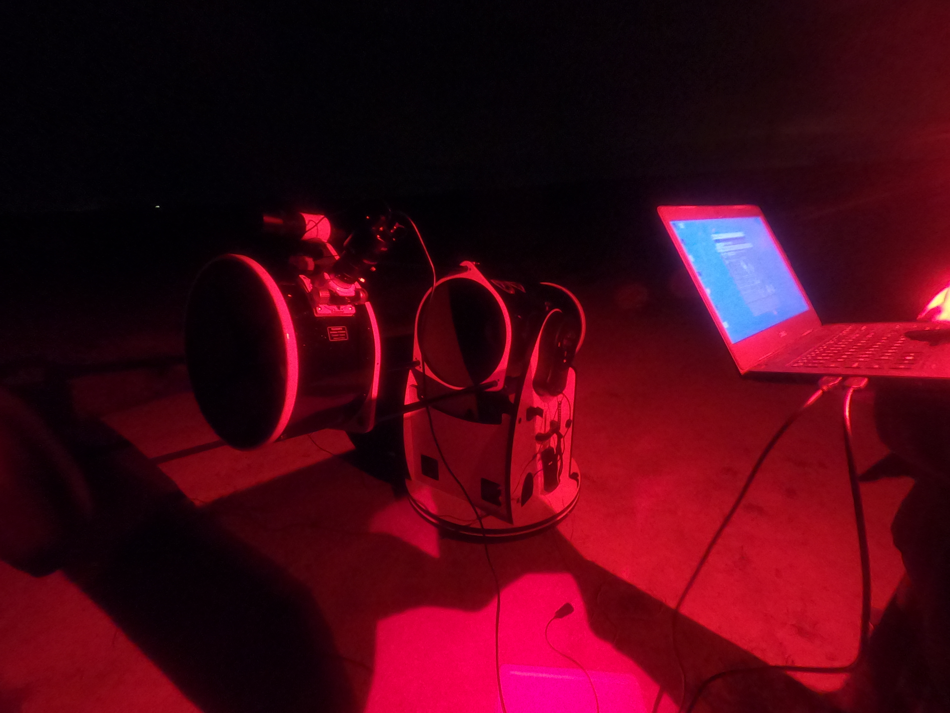Une télescope avec quelqu’un à côté qui tient un PC. Tout est éclairé par une lumière rouge