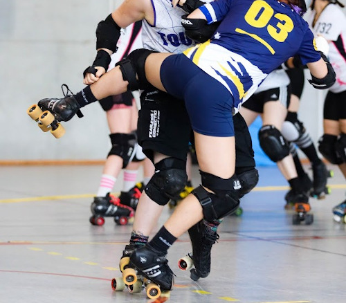 Un match de roller derby. Quelqu’un bloque un.e adversaire avec sa cuisse.