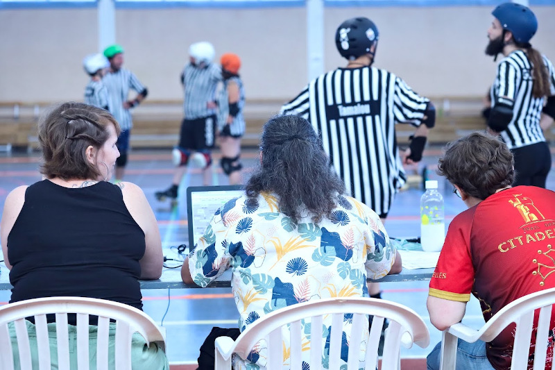 Des arbitres à la table de score. On voit des arbitres en rayures sur la track devant.