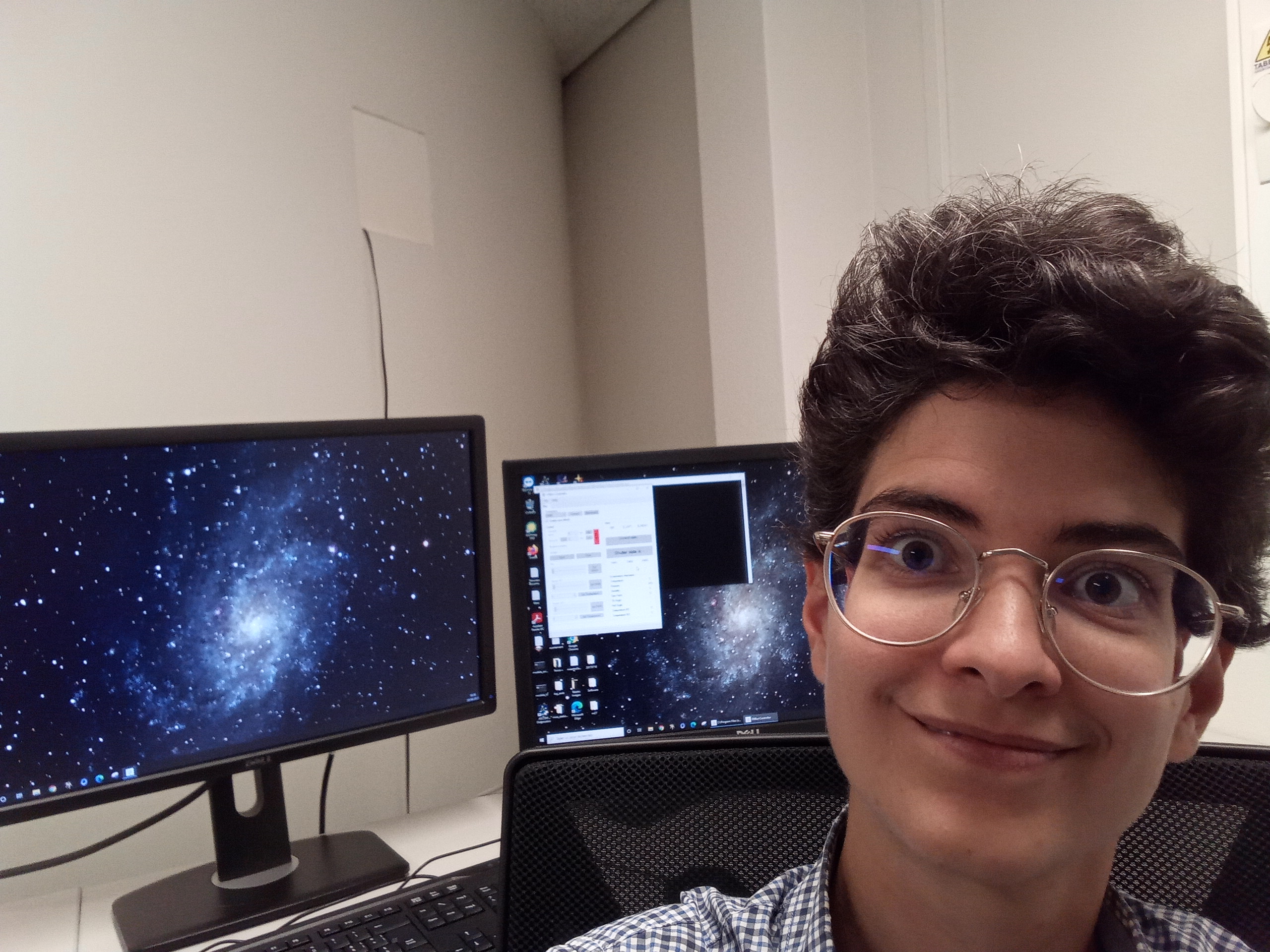 Ma tête devant les deux écrans de l'ordinateur. Le fond d'écran représente une galaxie spirale.